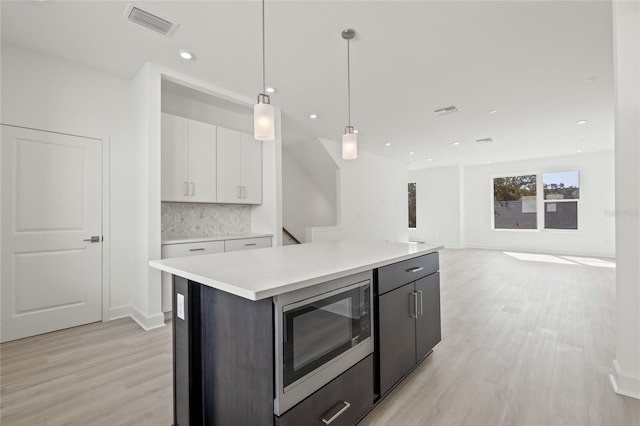 kitchen with visible vents, white cabinetry, light wood-type flooring, tasteful backsplash, and stainless steel microwave