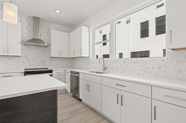 kitchen featuring tasteful backsplash, white cabinets, wall chimney exhaust hood, stainless steel appliances, and a sink