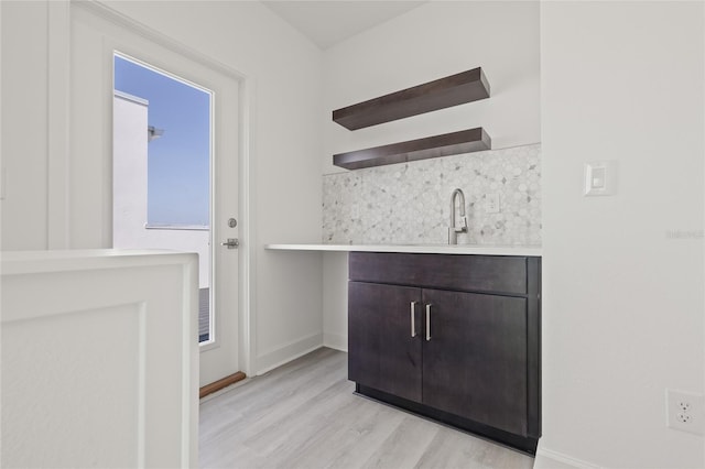 interior space featuring light wood-type flooring, a sink, baseboards, and backsplash