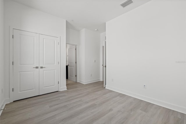 unfurnished bedroom featuring baseboards, a closet, visible vents, and light wood-style floors