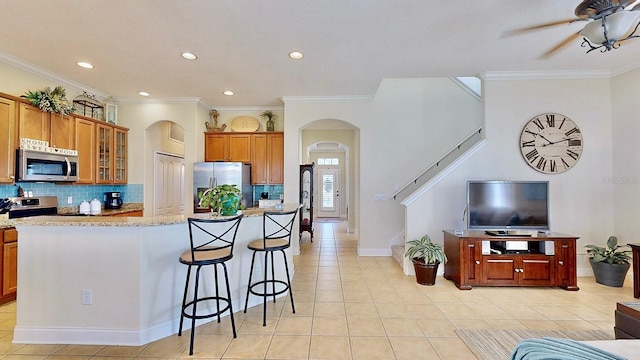 kitchen featuring appliances with stainless steel finishes, brown cabinetry, glass insert cabinets, and decorative backsplash