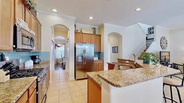 kitchen featuring a kitchen island with sink, arched walkways, stainless steel appliances, and a sink