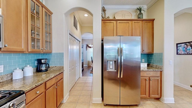 kitchen with arched walkways, stainless steel refrigerator with ice dispenser, glass insert cabinets, and light stone countertops