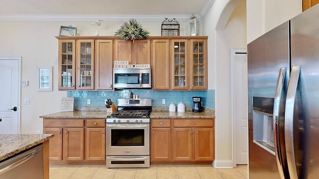 kitchen with glass insert cabinets, light stone countertops, appliances with stainless steel finishes, and ornamental molding