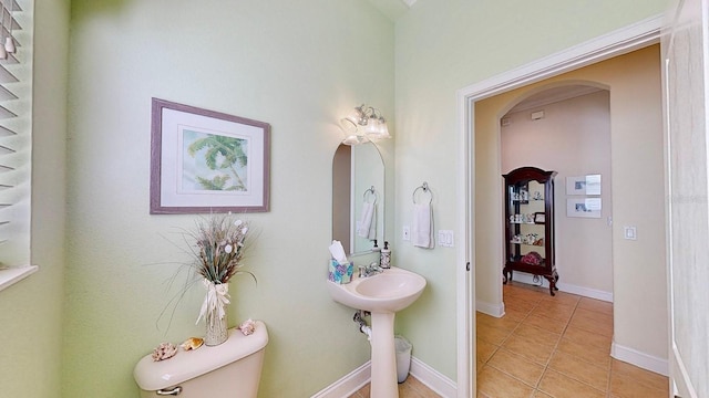 half bath featuring tile patterned flooring, toilet, and baseboards