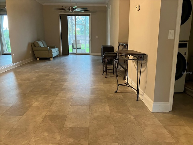 sitting room featuring a ceiling fan, stacked washer and clothes dryer, and baseboards