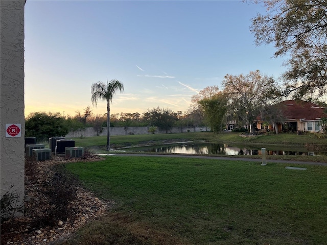 yard at dusk with central AC unit and a water view