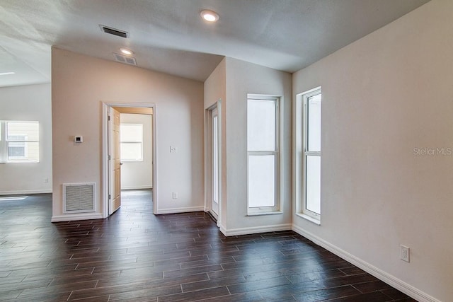 empty room with visible vents, vaulted ceiling, and dark wood-style flooring