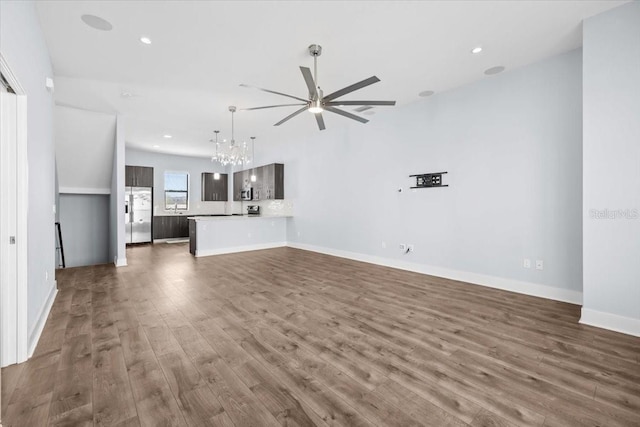 unfurnished living room featuring dark wood-type flooring, recessed lighting, baseboards, and ceiling fan with notable chandelier