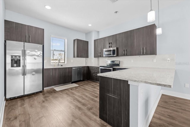 kitchen featuring light wood finished floors, appliances with stainless steel finishes, a sink, dark brown cabinets, and a peninsula