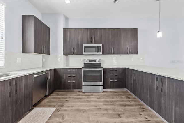 kitchen with tasteful backsplash, appliances with stainless steel finishes, hanging light fixtures, dark brown cabinets, and light wood-style floors