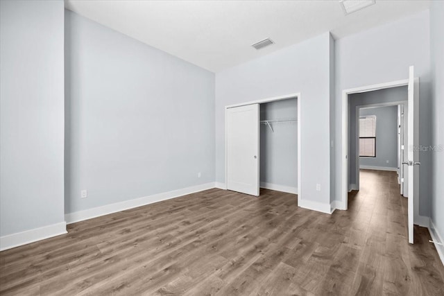 unfurnished bedroom featuring a closet, wood finished floors, visible vents, and baseboards