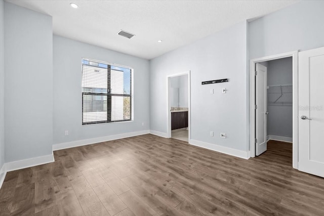 unfurnished bedroom with a walk in closet, dark wood finished floors, and baseboards