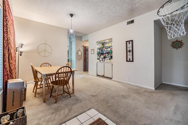 dining room with light carpet, a textured ceiling, visible vents, and baseboards