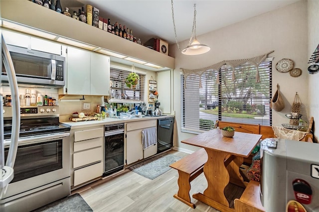 kitchen featuring light wood finished floors, white cabinets, appliances with stainless steel finishes, hanging light fixtures, and light countertops