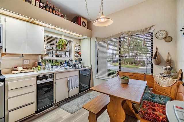 kitchen featuring white cabinets, light countertops, light wood-type flooring, dishwasher, and decorative light fixtures