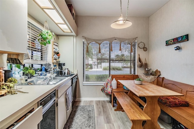 kitchen with decorative light fixtures, light wood finished floors, light countertops, white cabinets, and a sink