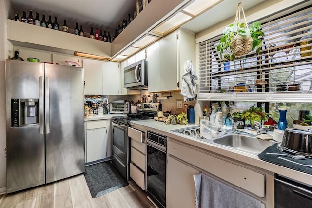 kitchen featuring light countertops, appliances with stainless steel finishes, white cabinetry, a sink, and light wood-type flooring