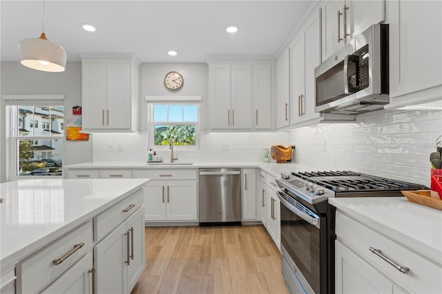 kitchen with light wood finished floors, appliances with stainless steel finishes, a sink, and white cabinets