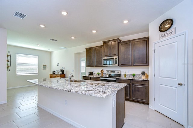 kitchen featuring visible vents, appliances with stainless steel finishes, light tile patterned flooring, a sink, and an island with sink