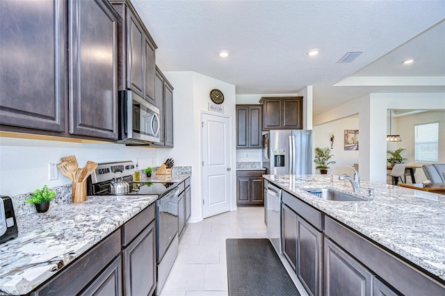 kitchen with dark brown cabinetry, visible vents, appliances with stainless steel finishes, light stone counters, and a sink