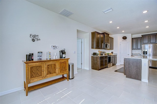 kitchen with a center island with sink, visible vents, stainless steel appliances, and dark brown cabinets