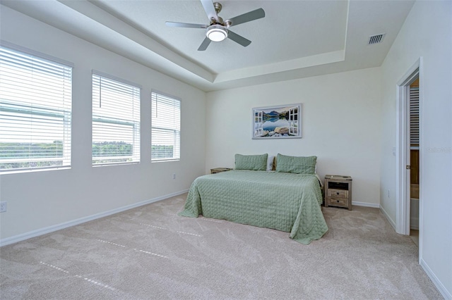 bedroom featuring light carpet, baseboards, visible vents, a raised ceiling, and a ceiling fan