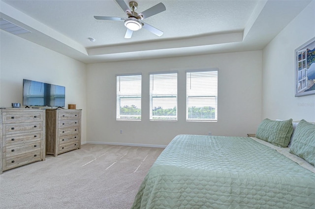 bedroom featuring light carpet, multiple windows, and a tray ceiling