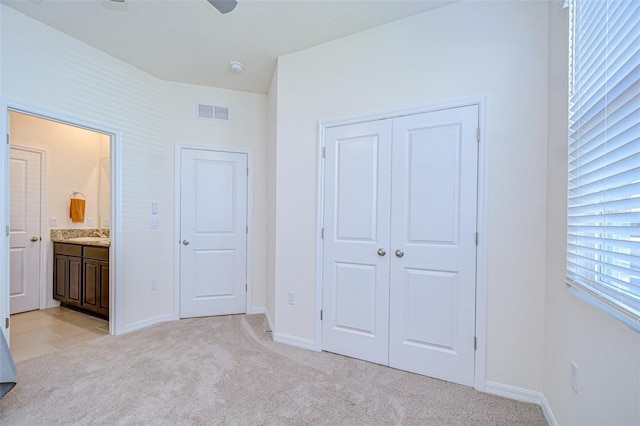 unfurnished bedroom with a closet, visible vents, light carpet, ensuite bath, and baseboards