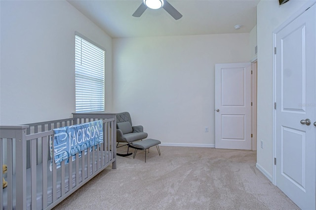 bedroom with a nursery area, ceiling fan, baseboards, and light colored carpet