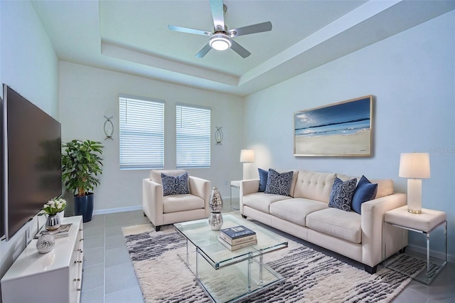 living room with a ceiling fan, a raised ceiling, light tile patterned flooring, and baseboards