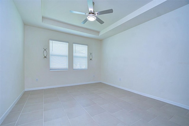 spare room with a raised ceiling, light tile patterned flooring, ceiling fan, and baseboards