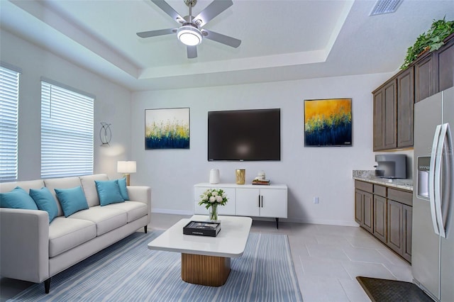 living area with a ceiling fan, visible vents, a tray ceiling, and baseboards