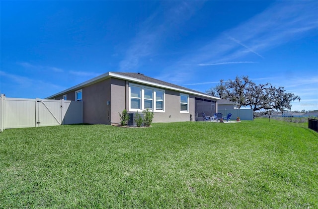 rear view of house featuring a lawn, a fenced backyard, a gate, and stucco siding