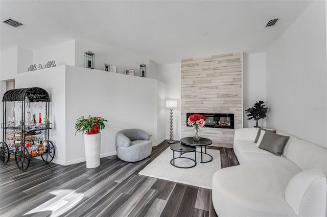 living area with a tile fireplace, visible vents, dark wood finished floors, and baseboards