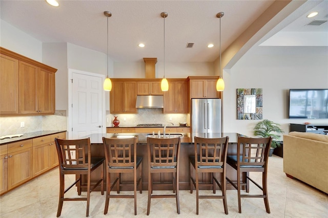 kitchen with a center island with sink, appliances with stainless steel finishes, open floor plan, under cabinet range hood, and a kitchen bar