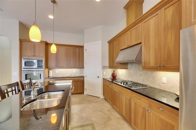 kitchen featuring under cabinet range hood, a sink, appliances with stainless steel finishes, dark stone counters, and decorative light fixtures