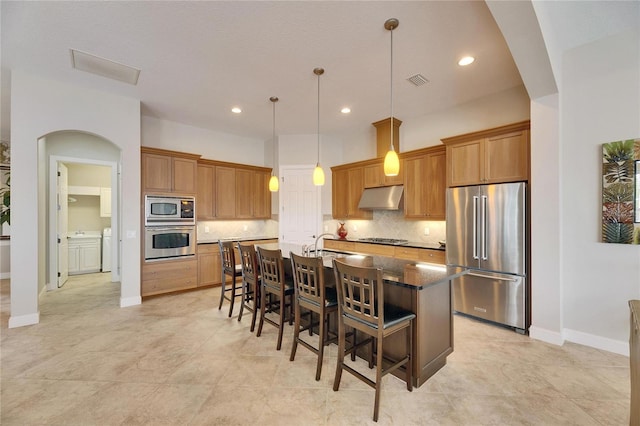 kitchen featuring a center island with sink, appliances with stainless steel finishes, a kitchen breakfast bar, decorative light fixtures, and under cabinet range hood