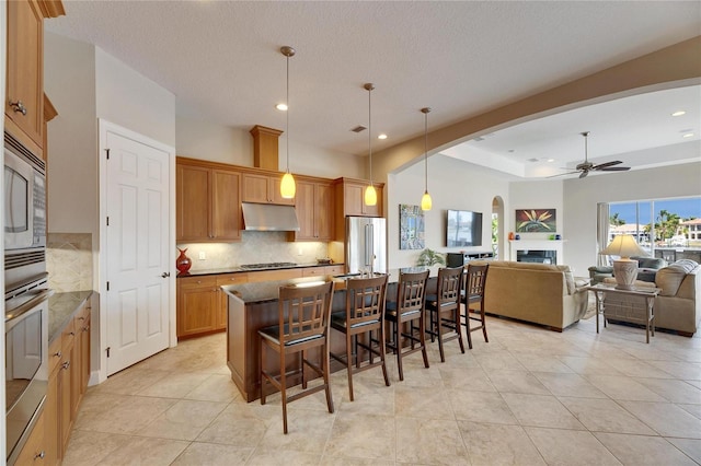 kitchen featuring hanging light fixtures, under cabinet range hood, stainless steel appliances, and open floor plan