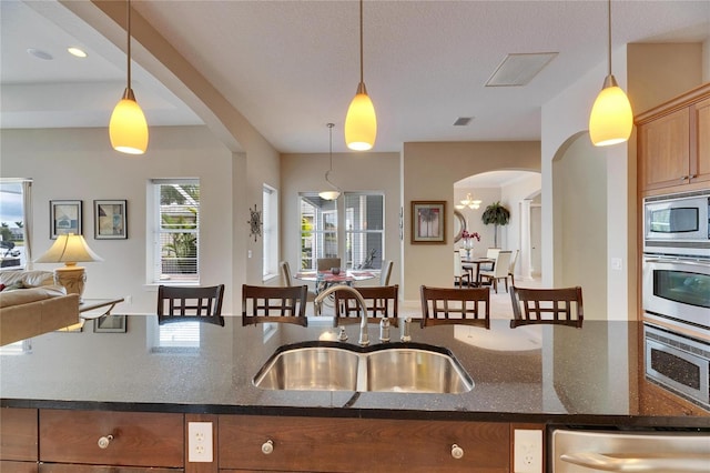 kitchen featuring hanging light fixtures, appliances with stainless steel finishes, open floor plan, and a sink