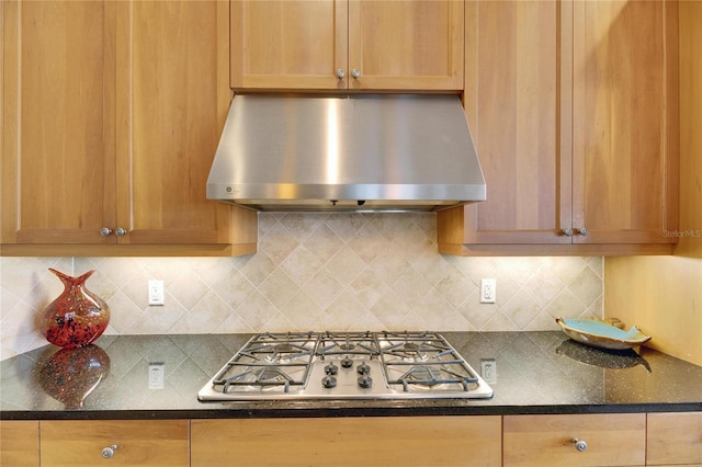 kitchen featuring extractor fan, backsplash, brown cabinets, dark stone countertops, and stainless steel gas stovetop