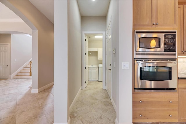 kitchen featuring baseboards, washer and clothes dryer, arched walkways, stainless steel appliances, and light brown cabinets