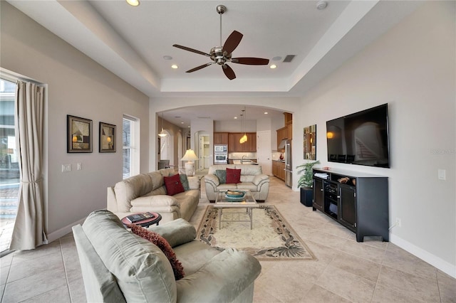 living room featuring arched walkways, a tray ceiling, visible vents, and baseboards