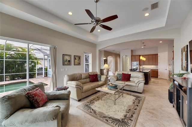 living area featuring arched walkways, a tray ceiling, visible vents, and recessed lighting