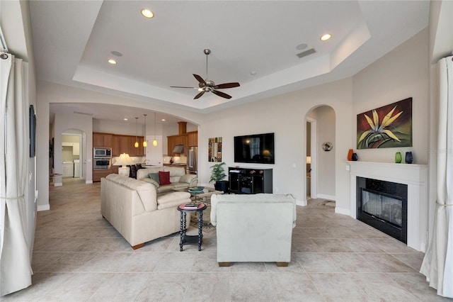 living area featuring arched walkways, a tray ceiling, a glass covered fireplace, and visible vents