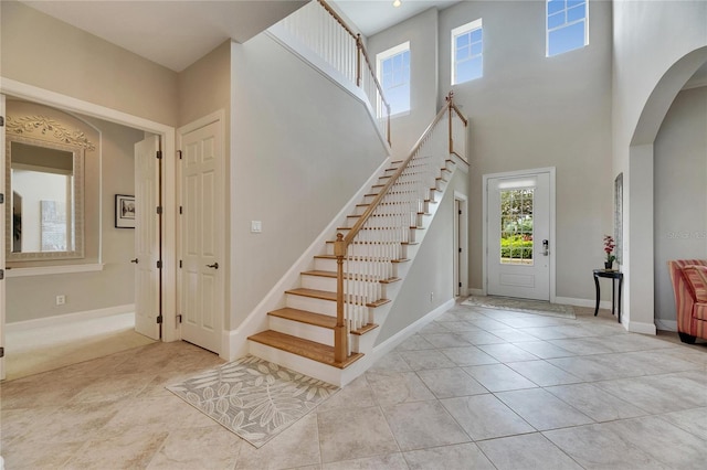 entryway featuring arched walkways, light tile patterned floors, a towering ceiling, baseboards, and stairway