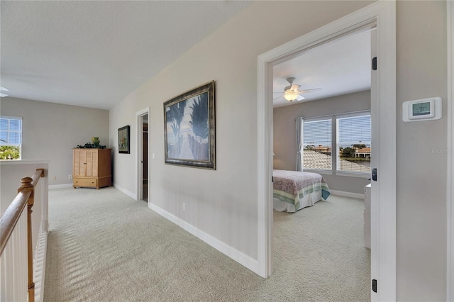 hall with an upstairs landing, light colored carpet, a textured ceiling, and baseboards