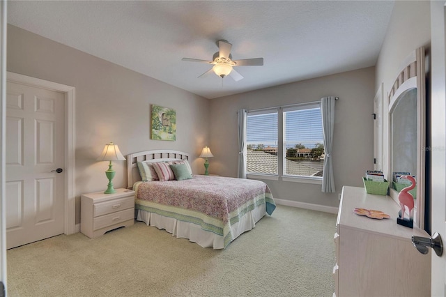 bedroom featuring light carpet, ceiling fan, baseboards, and a textured ceiling