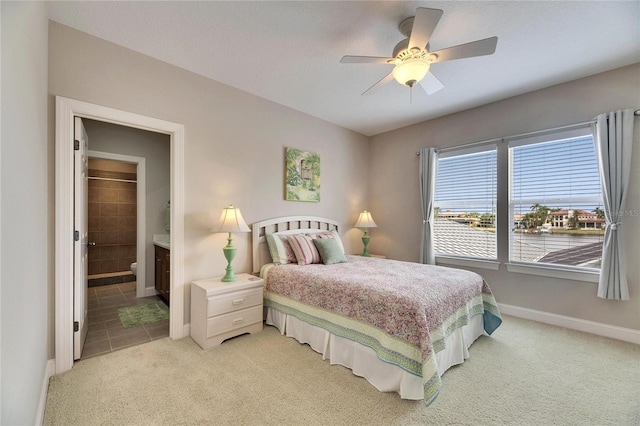 bedroom with baseboards, ensuite bath, a ceiling fan, and light colored carpet