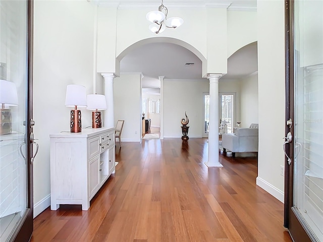 entrance foyer featuring baseboards, light wood-style flooring, decorative columns, arched walkways, and ornamental molding